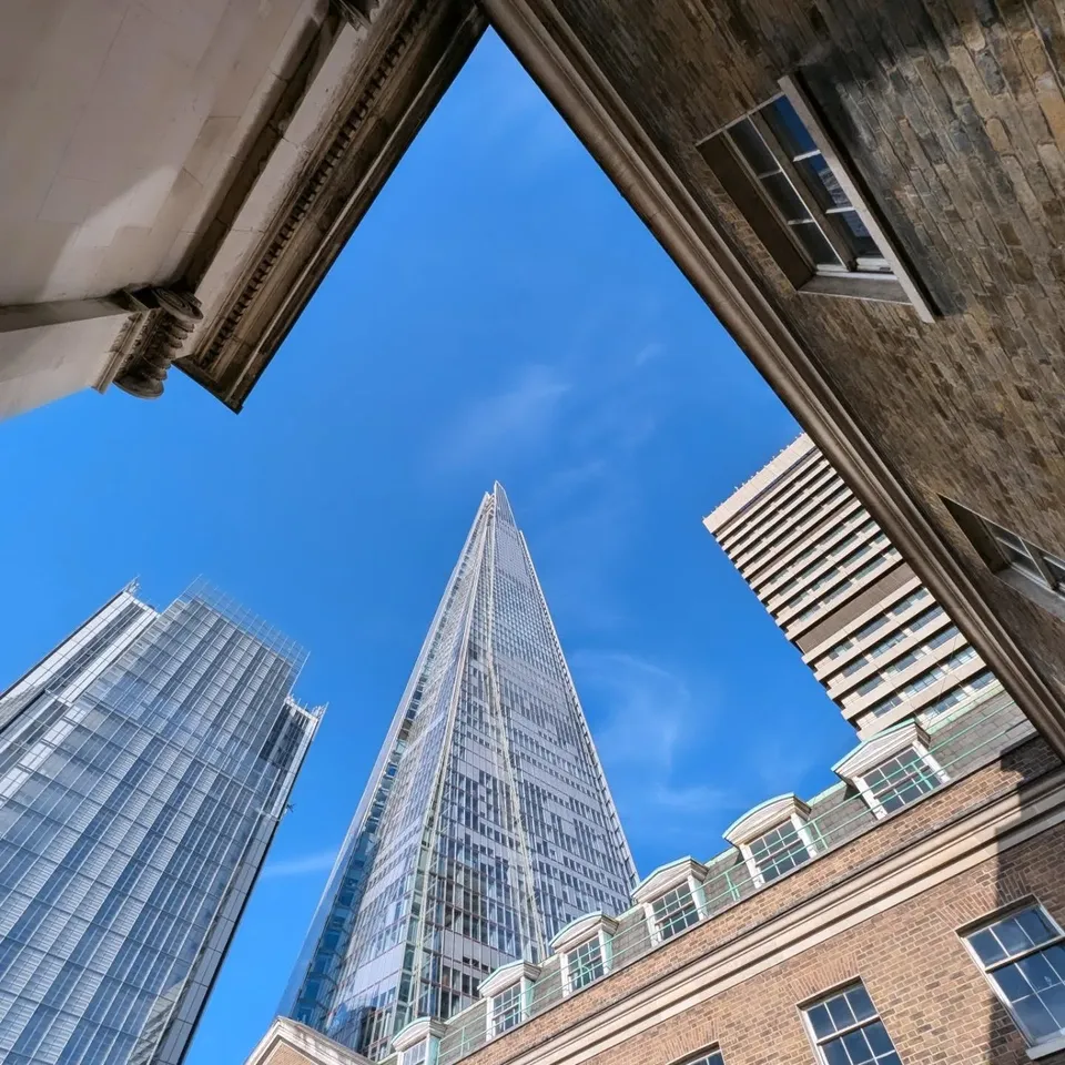 Looking straight up past brick buildings to the Shard against a blue sky