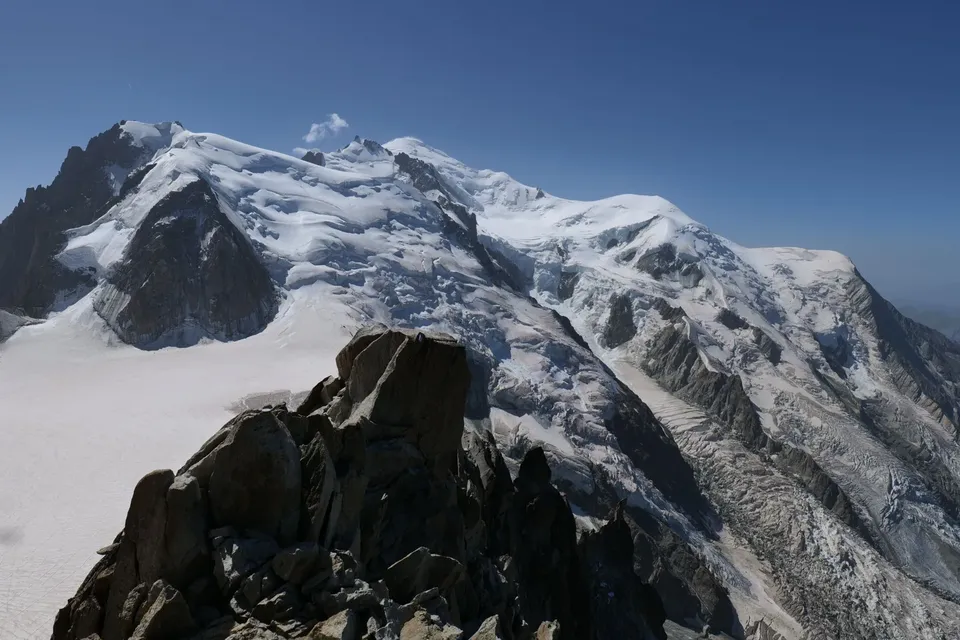 Snow-covered Mont Blanc massif and its glaciers behind a dark granite ridge